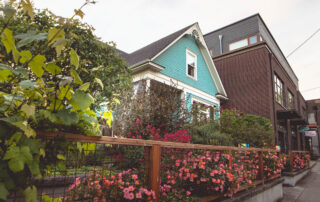 Aqua Green Home With Flowers And Vines Growing On Fence
