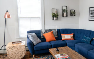 Colorful Room; Blue Couch, Orange & Grey Pillows, Wood Floor and Coffee Table, with a bright window